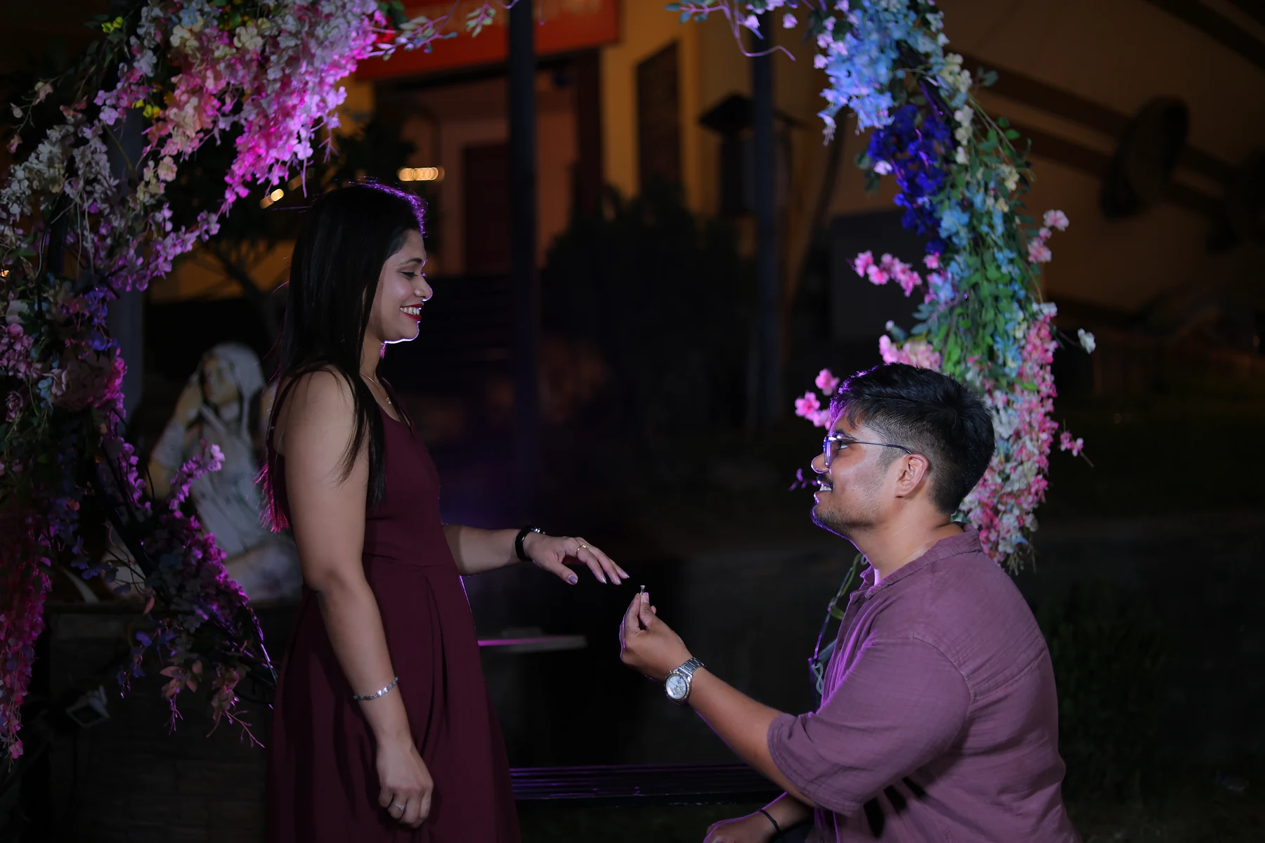 Rohan holding a ring for Ritika beneath a floral arch.